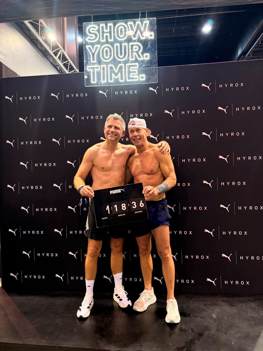Wojtek and Patrick at the HYROX Gdańsk 2026 finish line holding a time board reading 1:18:36